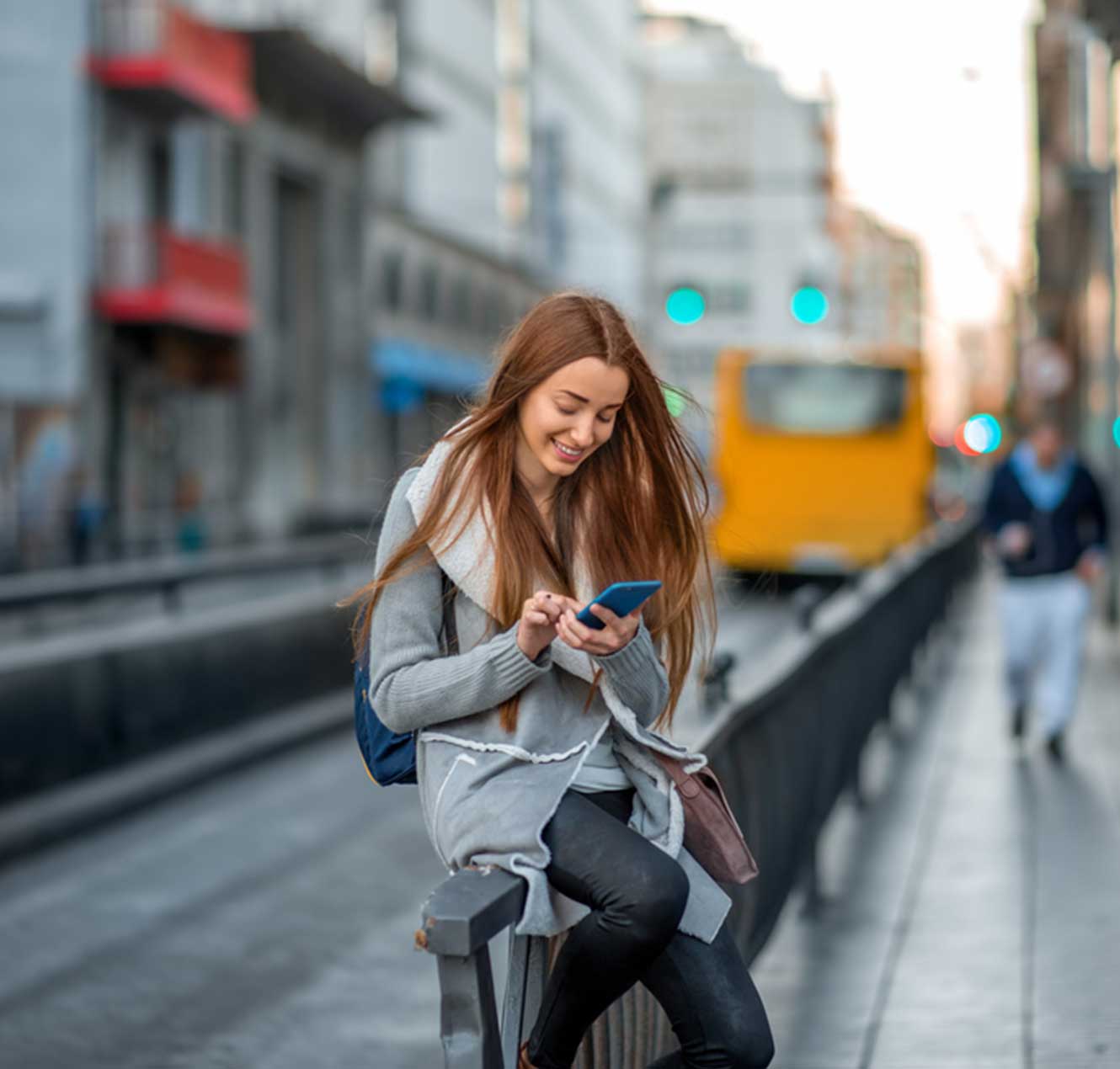 Young Lady Perched on a Railing, Smiling and Looking at Her Phone